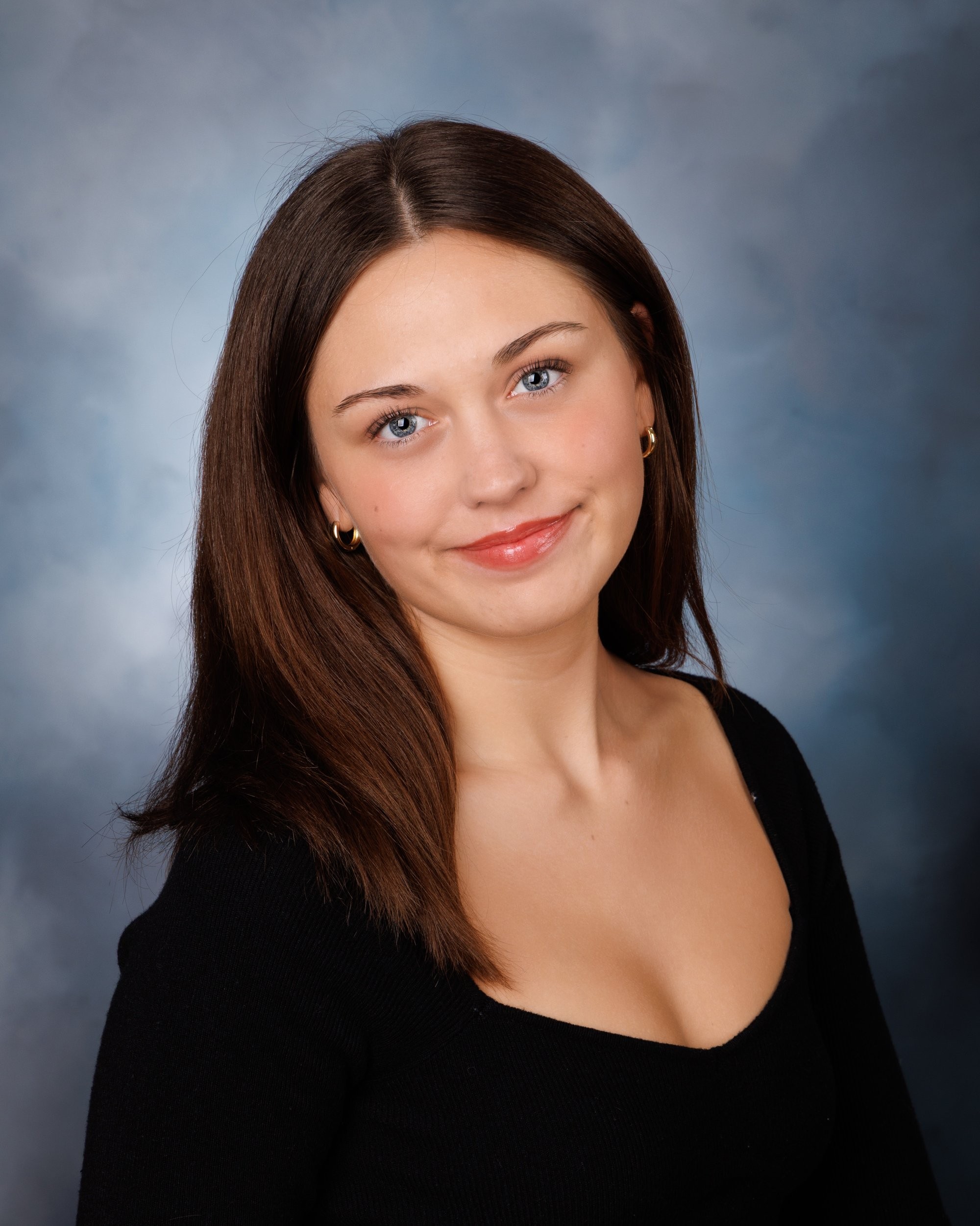Chloe's senior portrait with a subtle smile and black top against a blue studio background