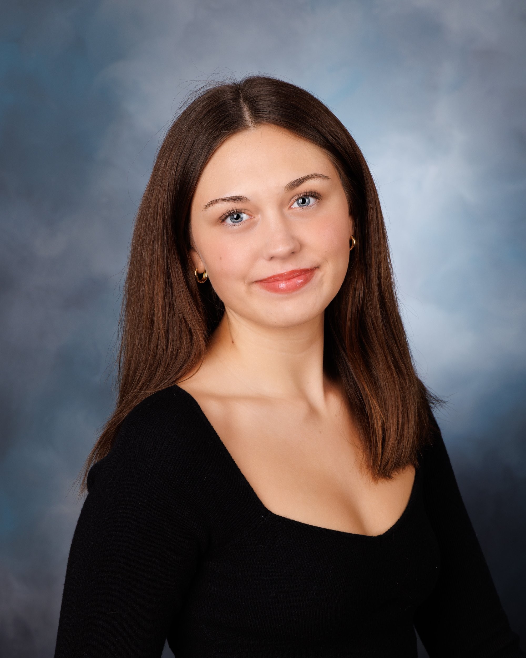 Chloe's senior portrait with a subtle smile and black top against a blue studio background