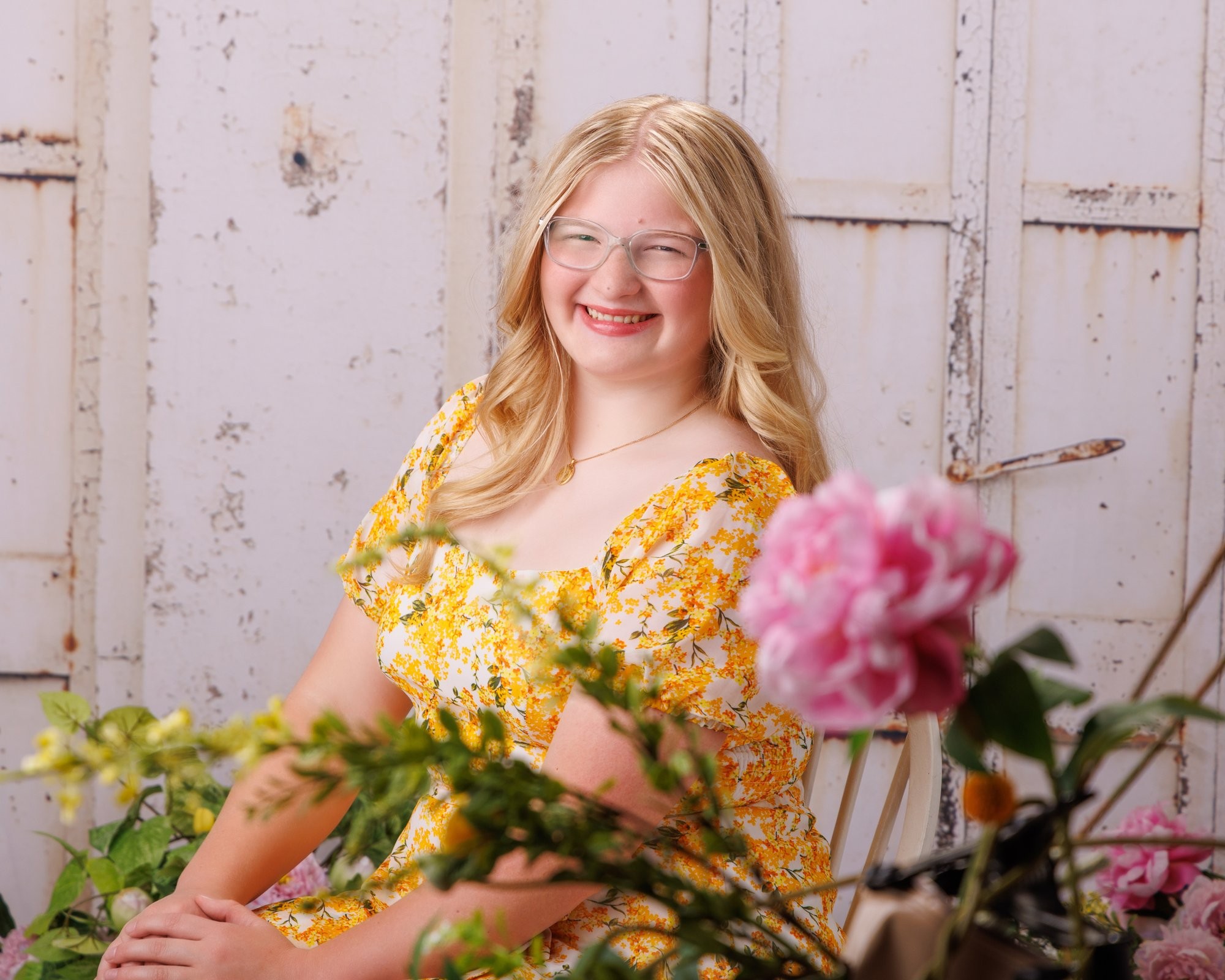Elizabeth seated on the floor in a yellow floral dress, smiling with flower arrangements nearby