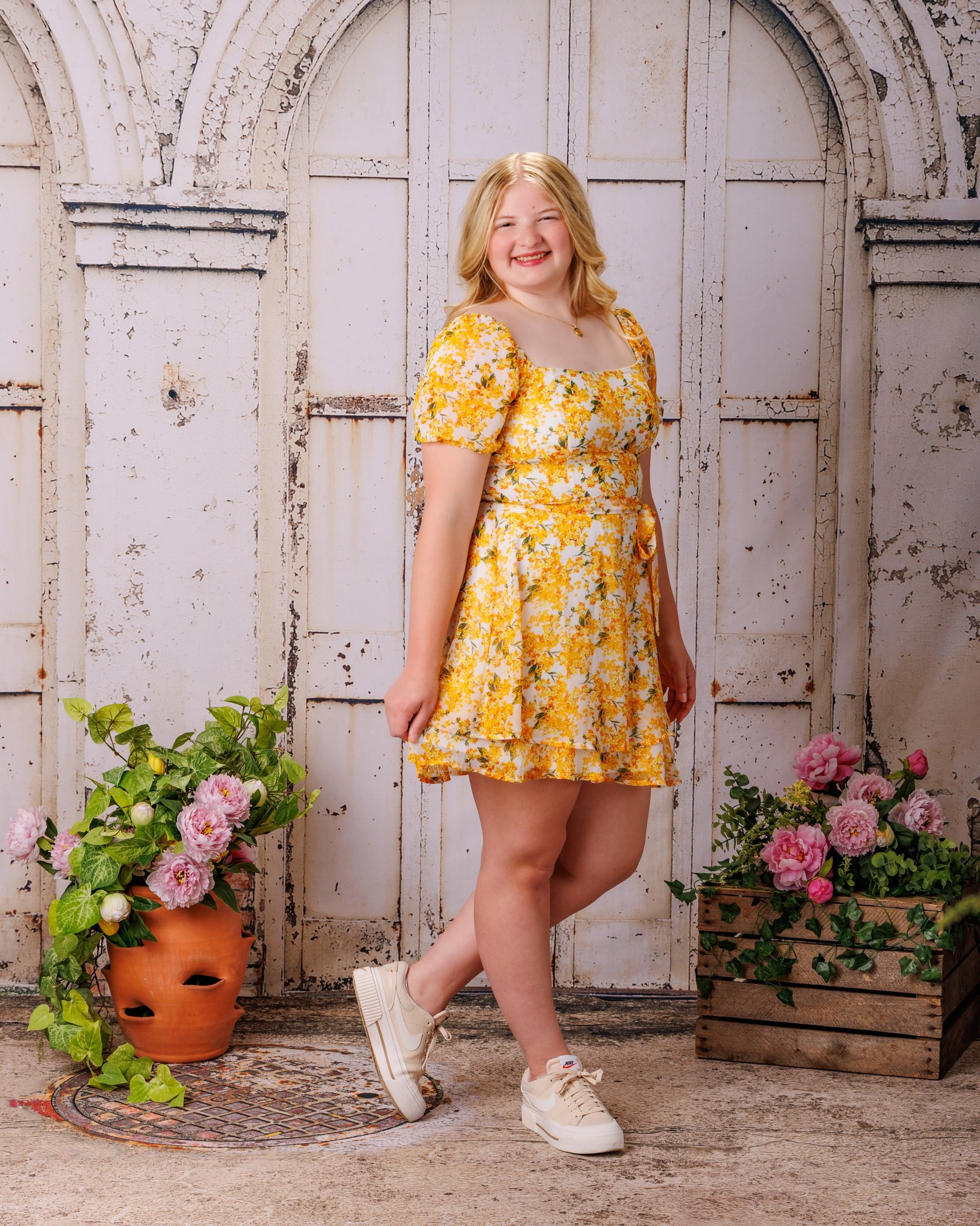 Elizabeth seated on the floor in a yellow floral dress, smiling with flower arrangements nearby