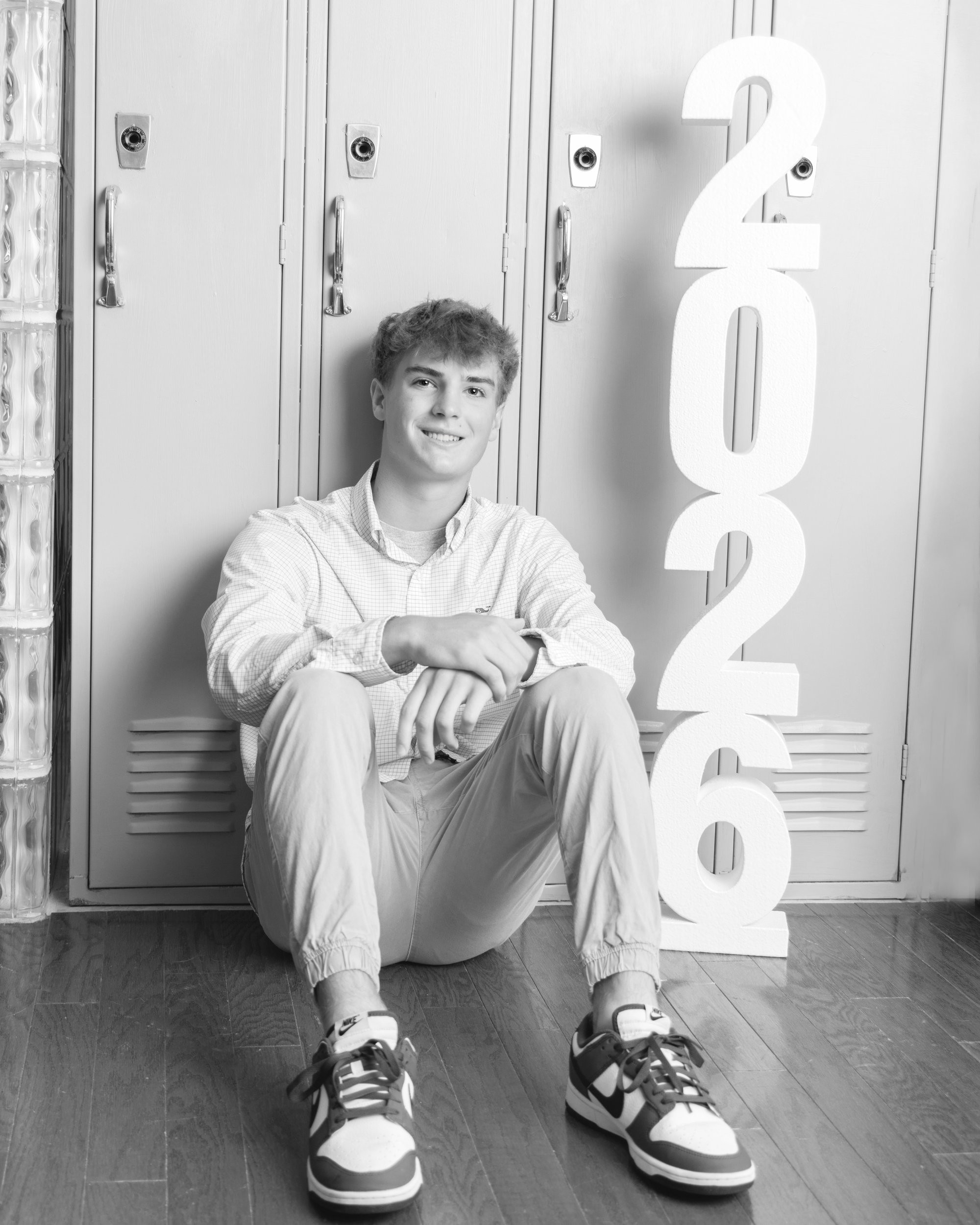 Jaxon seated against lockers with '2026' signage, Trenton senior photoshoot