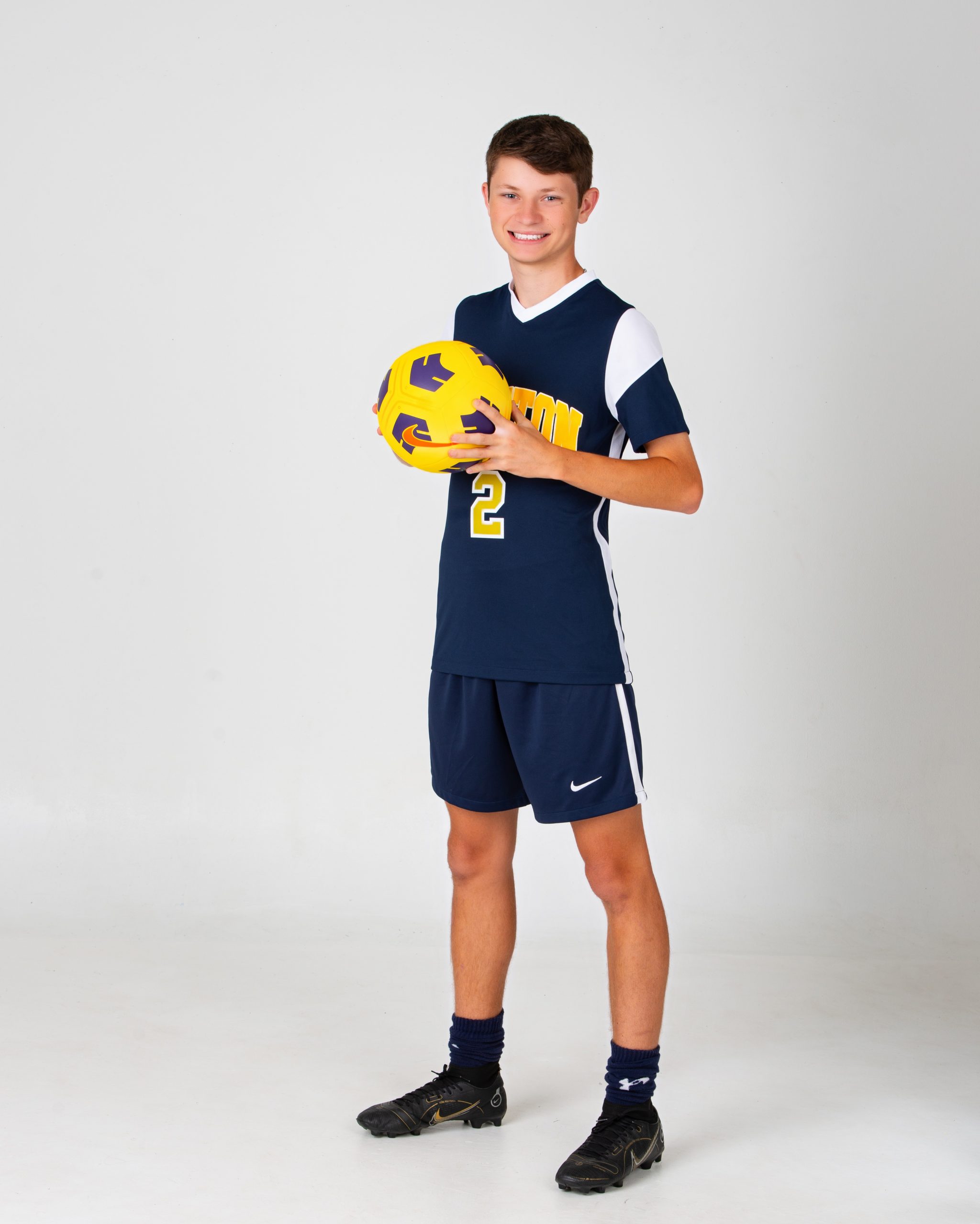 Senior male athlete holding yellow soccer ball in navy and gold uniform