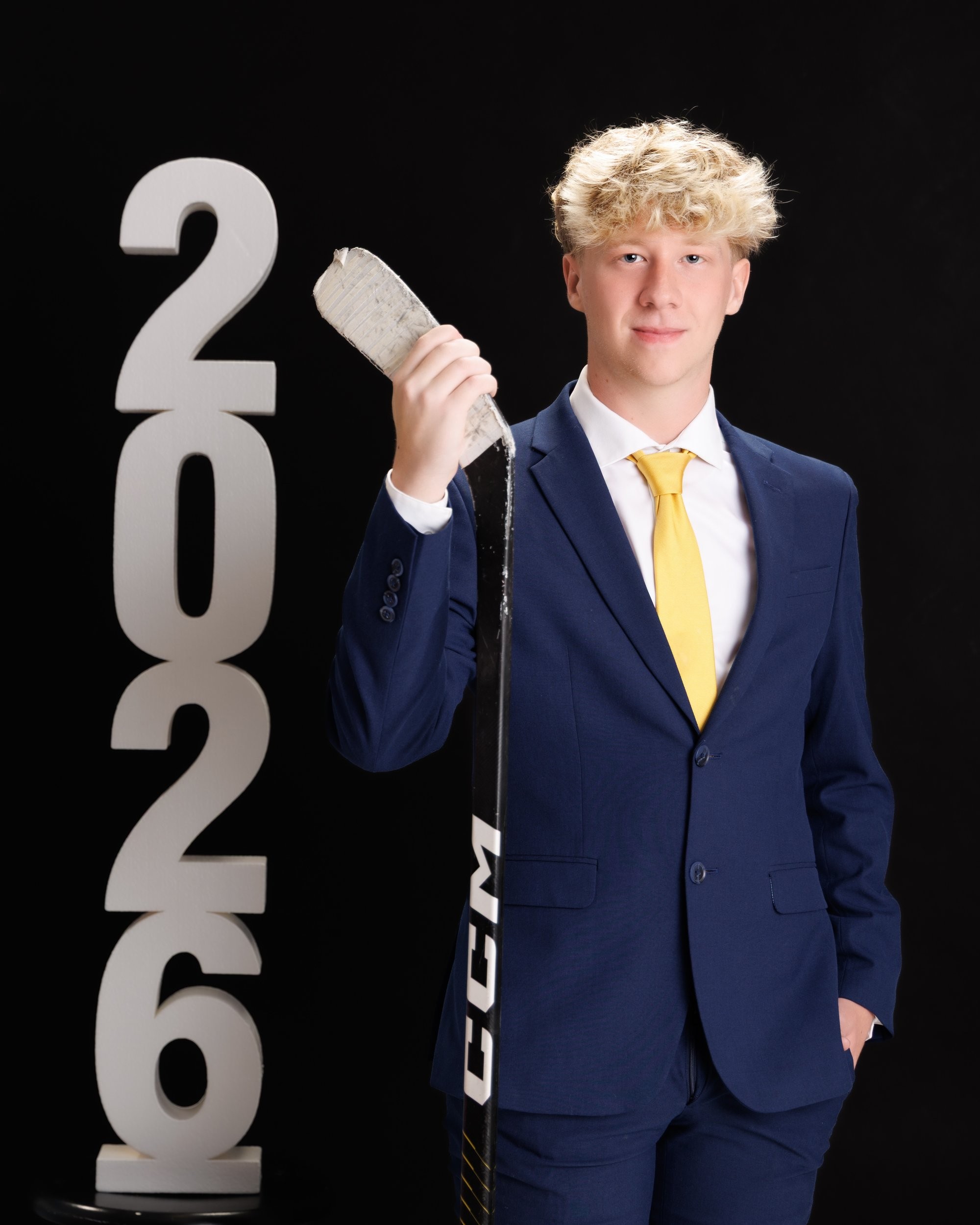 Trenton Senior Landon holding hockey stick and puck with '2026' backdrop