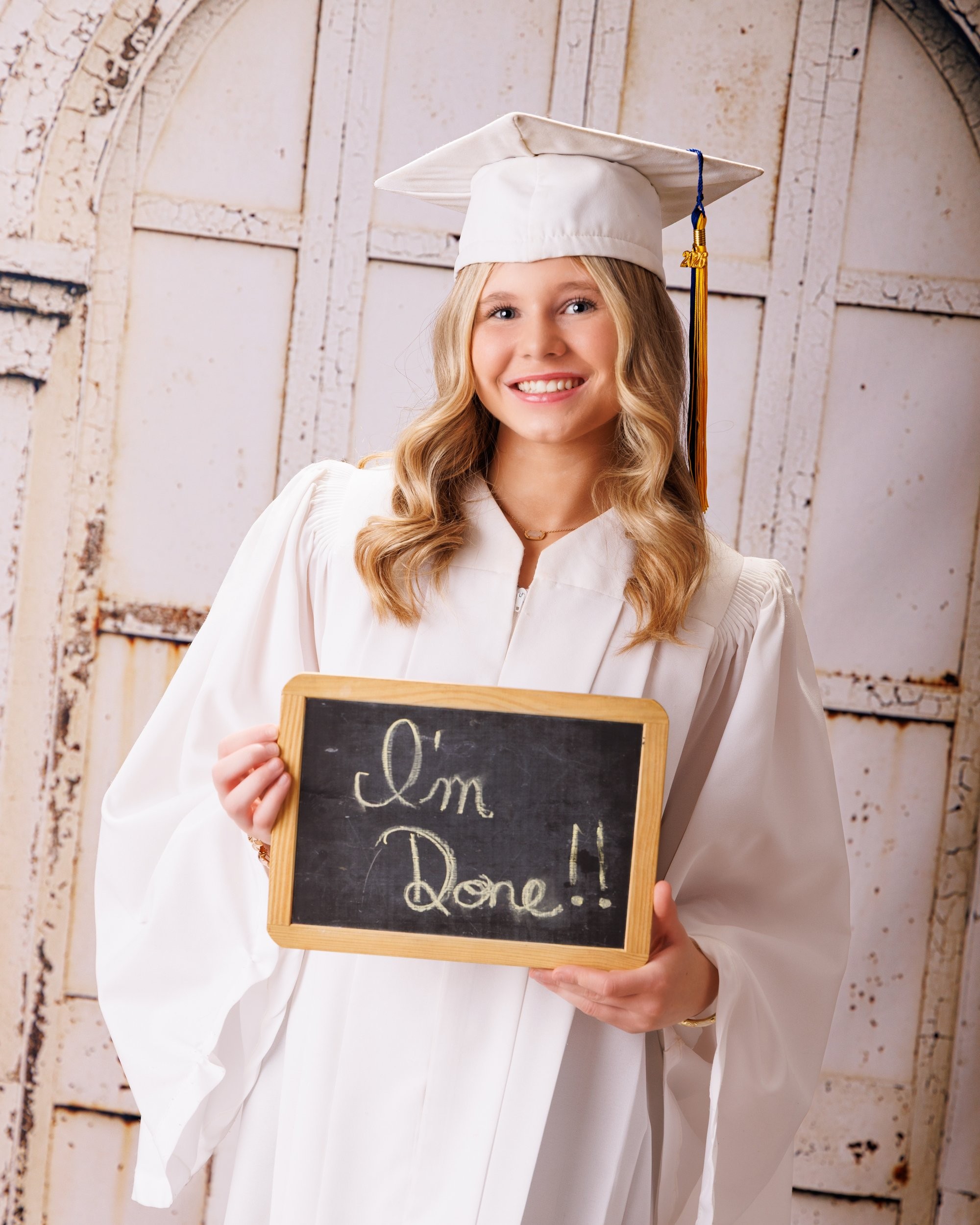 Trenton senior graduate McKenzie in a pink graduation gown with a 2023 tassel, smiling against a rustic backdrop
