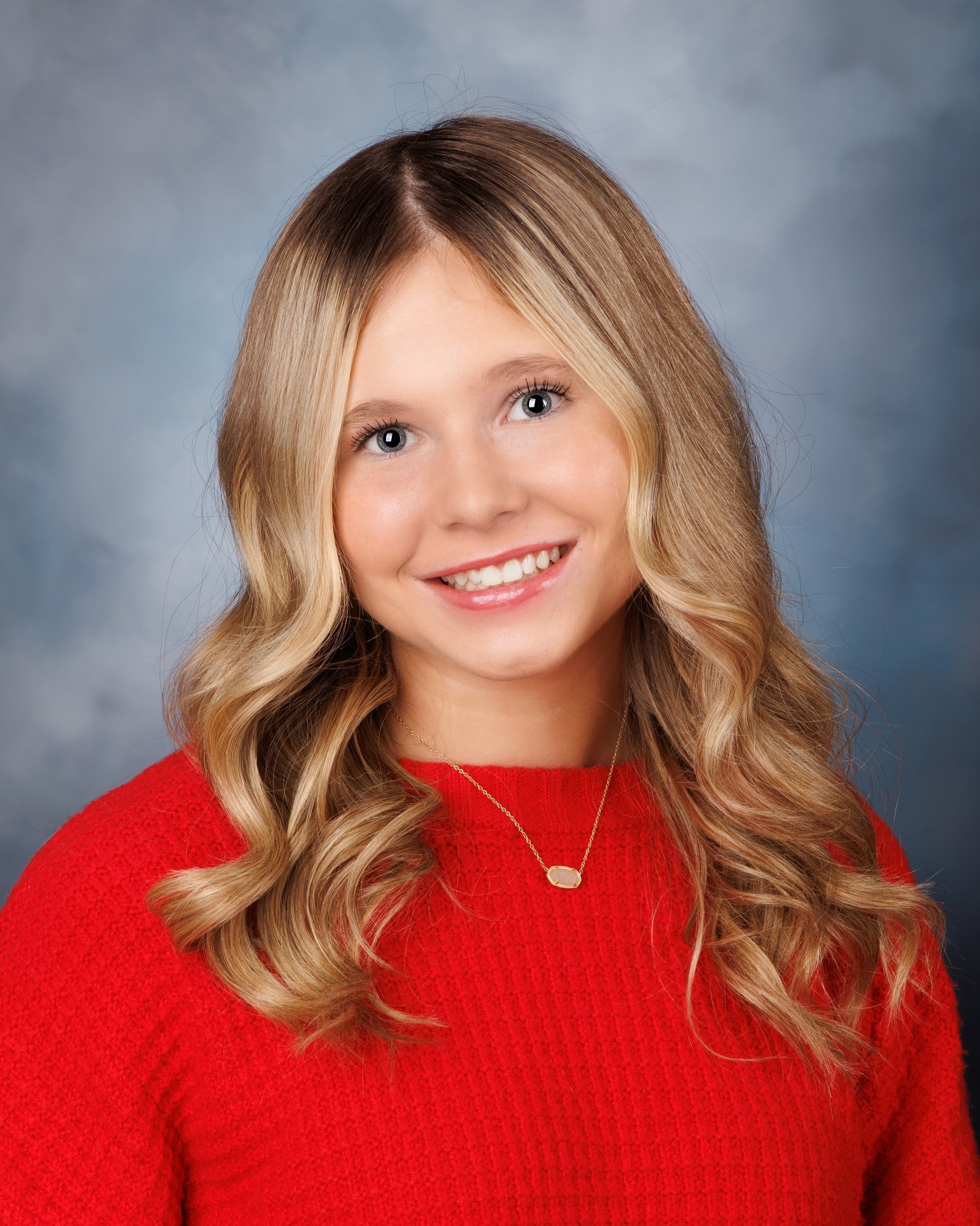 Trenton senior graduate McKenzie in a pink graduation gown with a 2023 tassel, smiling against a rustic backdrop
