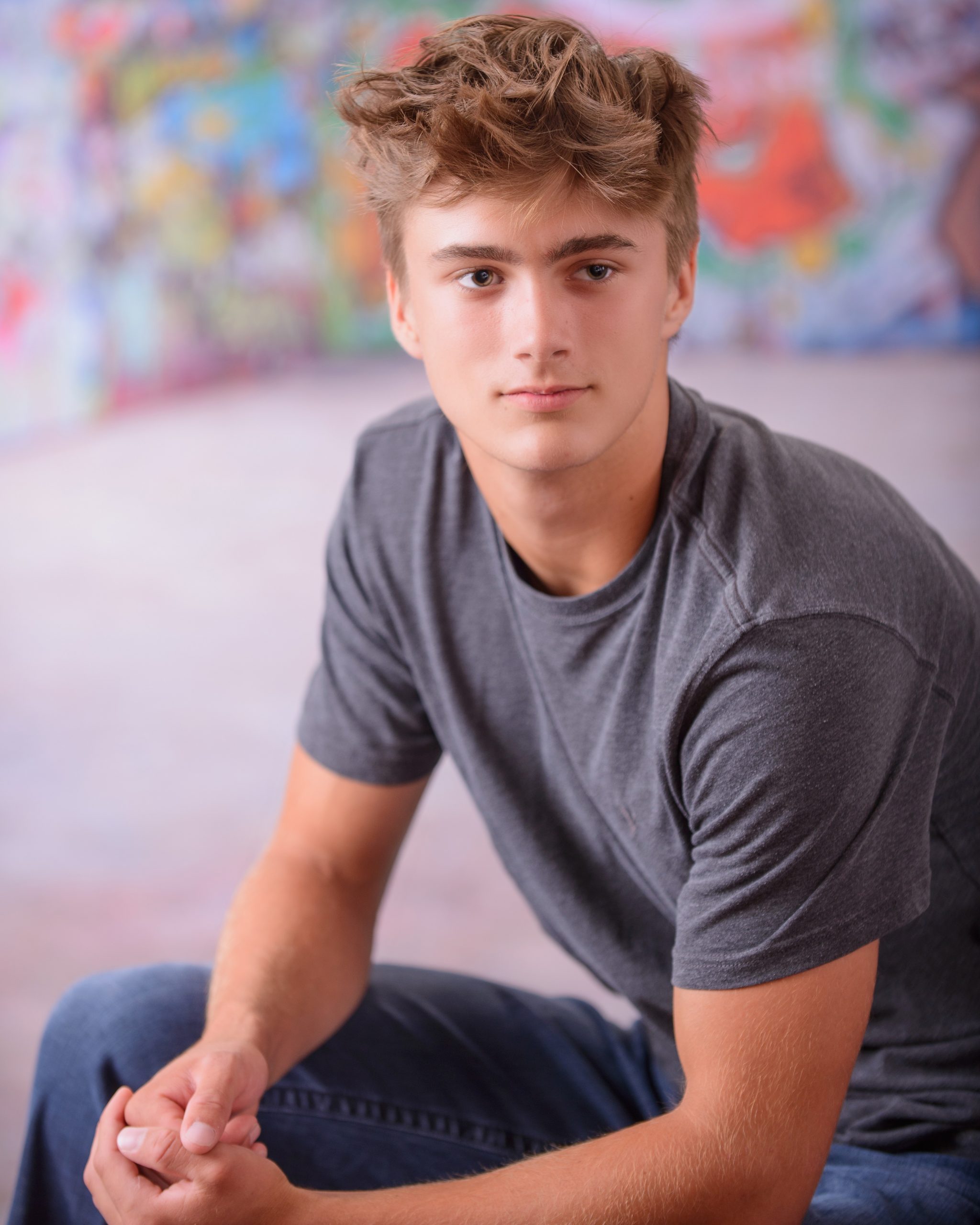 Casual Trenton senior session portrait showing a young man in layered clothing with a graffiti wall backdrop