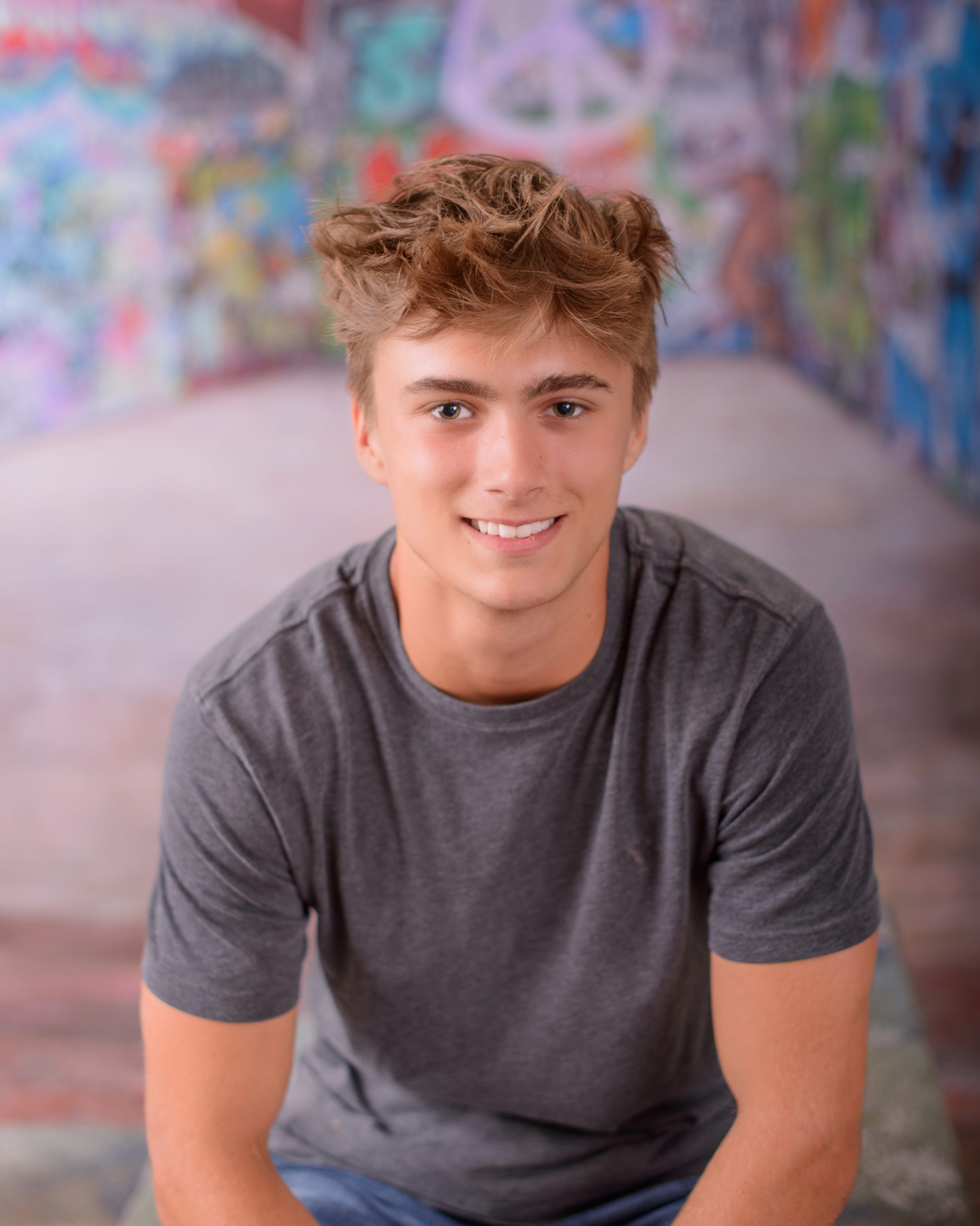 Casual Trenton senior session portrait showing a young man in layered clothing with a graffiti wall backdrop