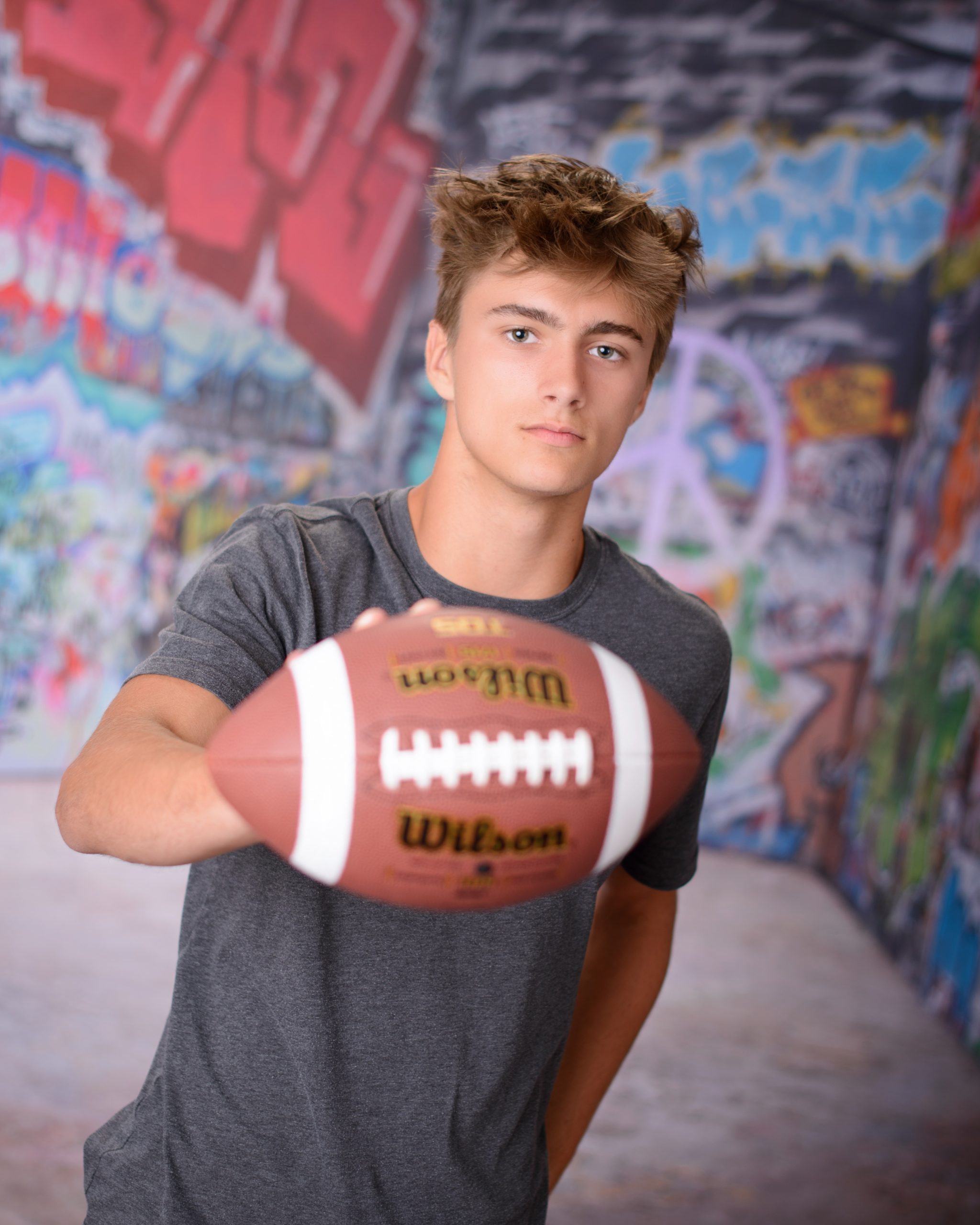 Casual Trenton senior session portrait showing a young man in layered clothing with a graffiti wall backdrop