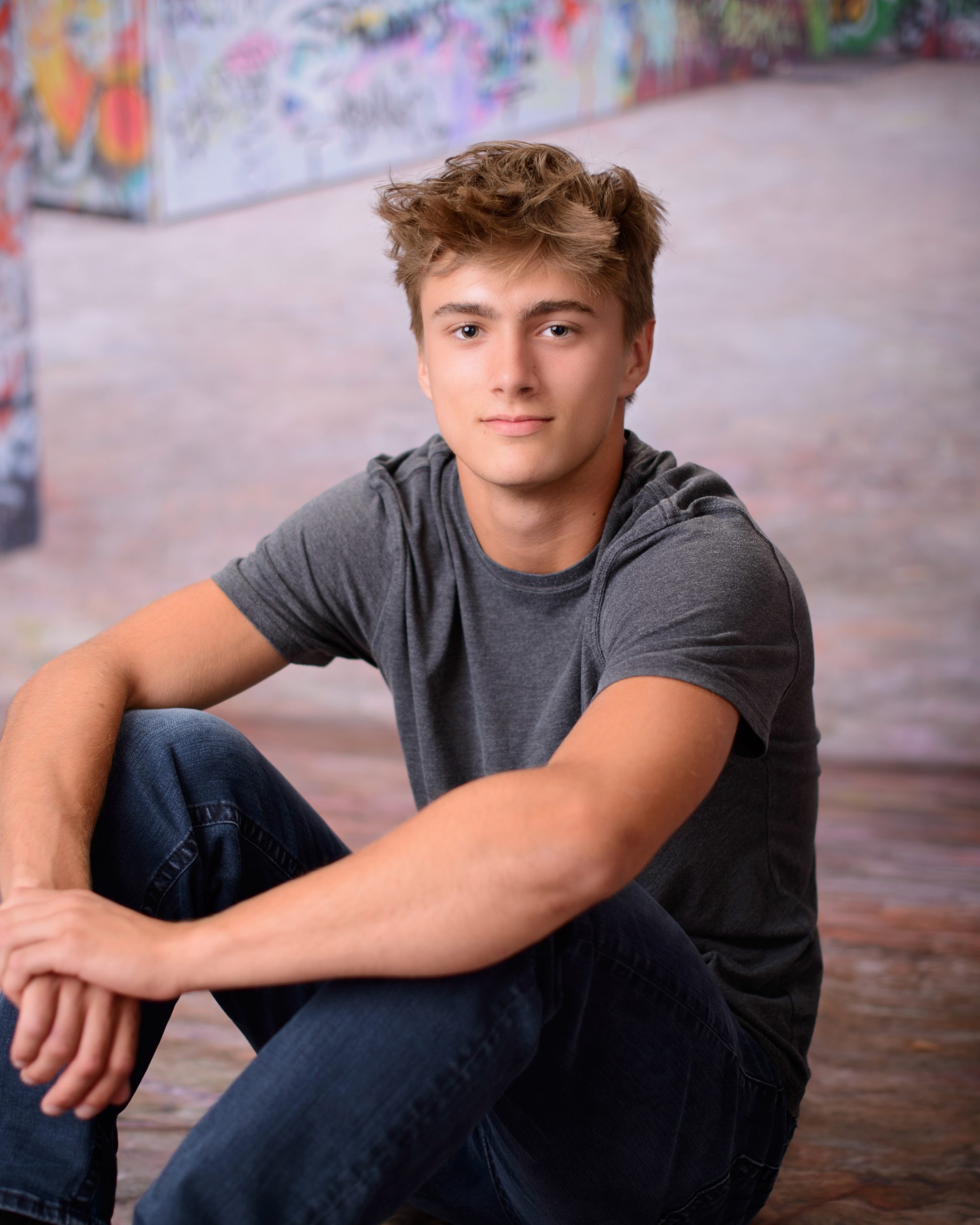 Casual Trenton senior session portrait showing a young man in layered clothing with a graffiti wall backdrop