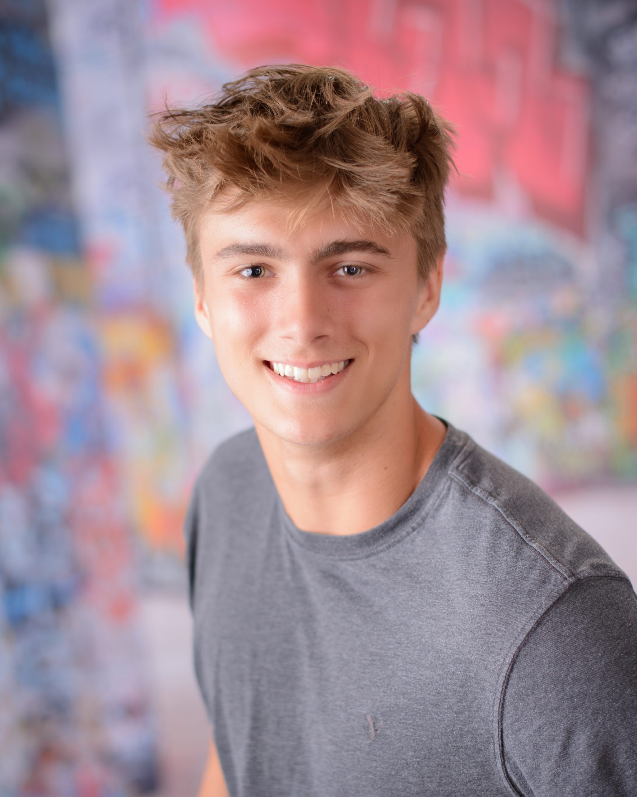 Casual Trenton senior session portrait showing a young man in layered clothing with a graffiti wall backdrop