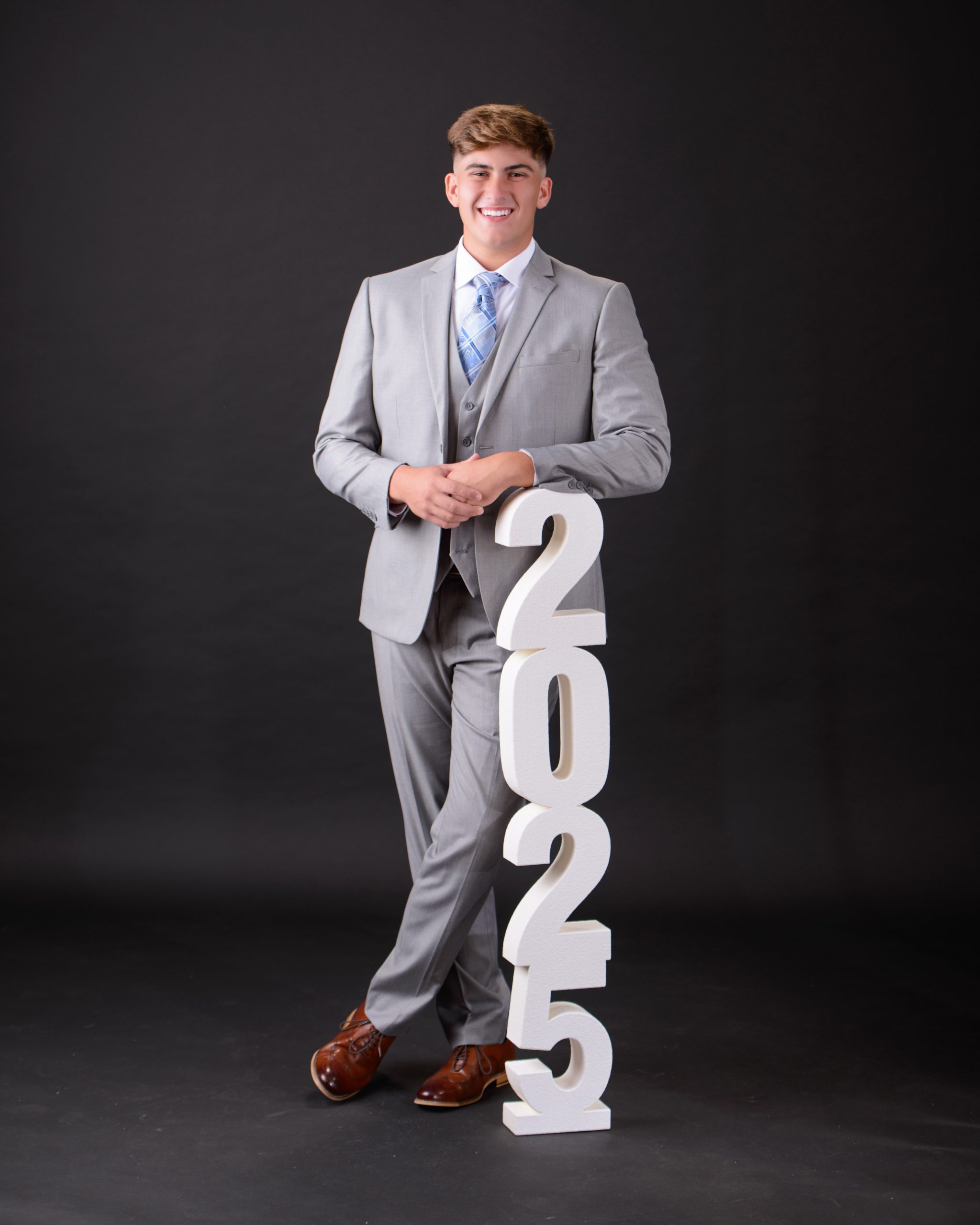 Trenton senior student posing with '2025' numbers in gray suit during studio photo session