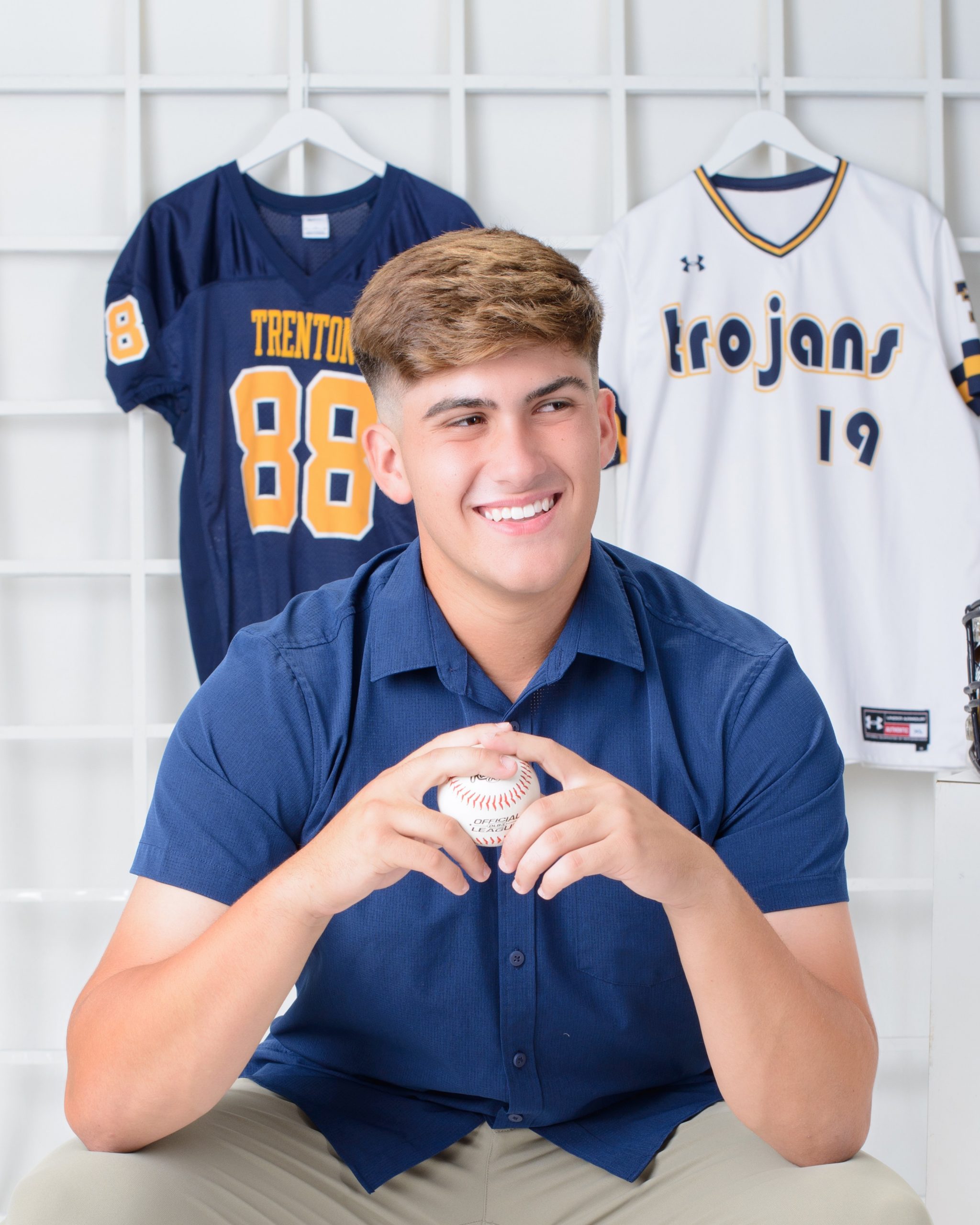 Student holding baseball in front of Trenton Trojans jerseys for high school senior photography