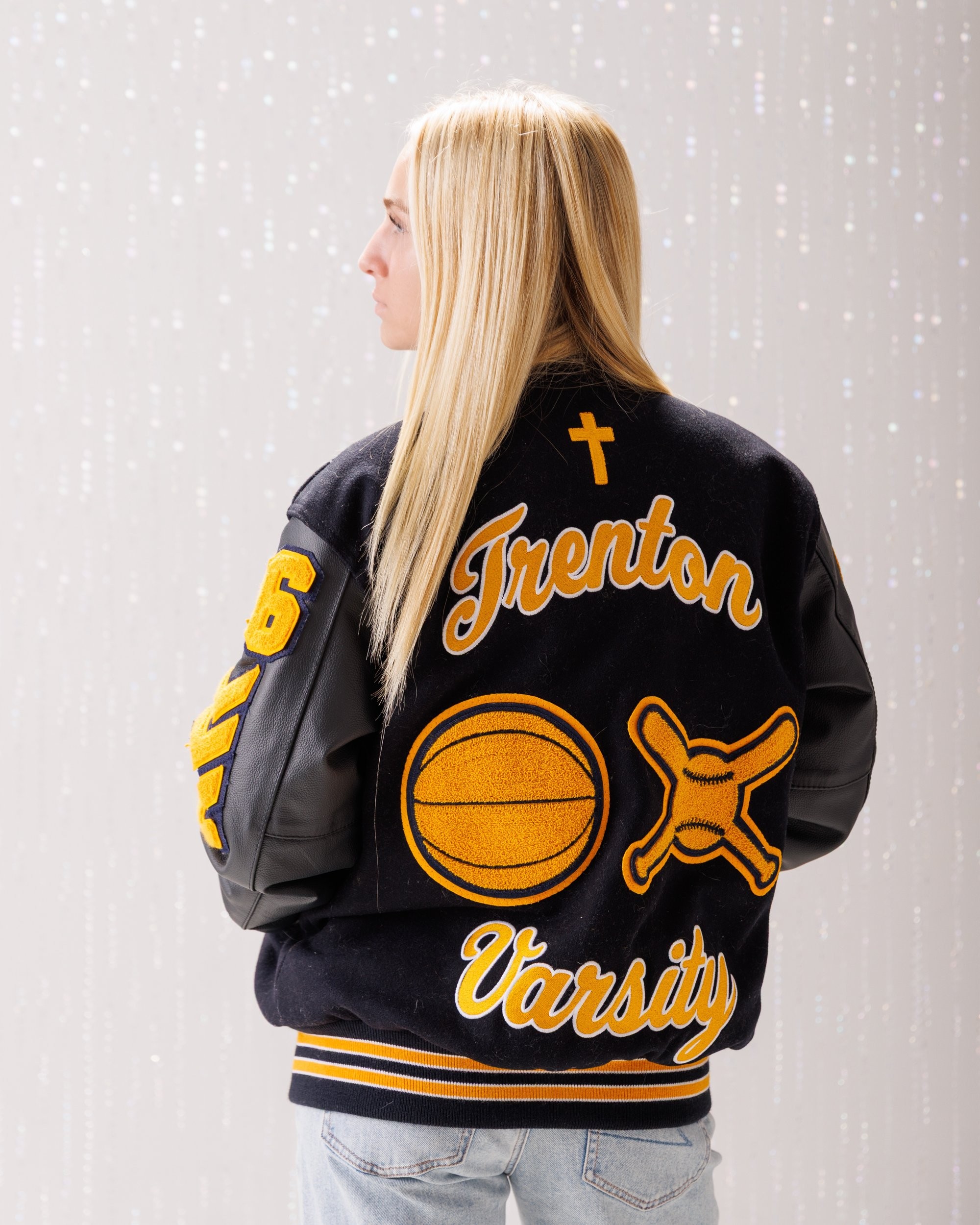 Back view of Alencia's Trenton Varsity jacket featuring 'Trenton' and 'Varsity' lettering with sports logos