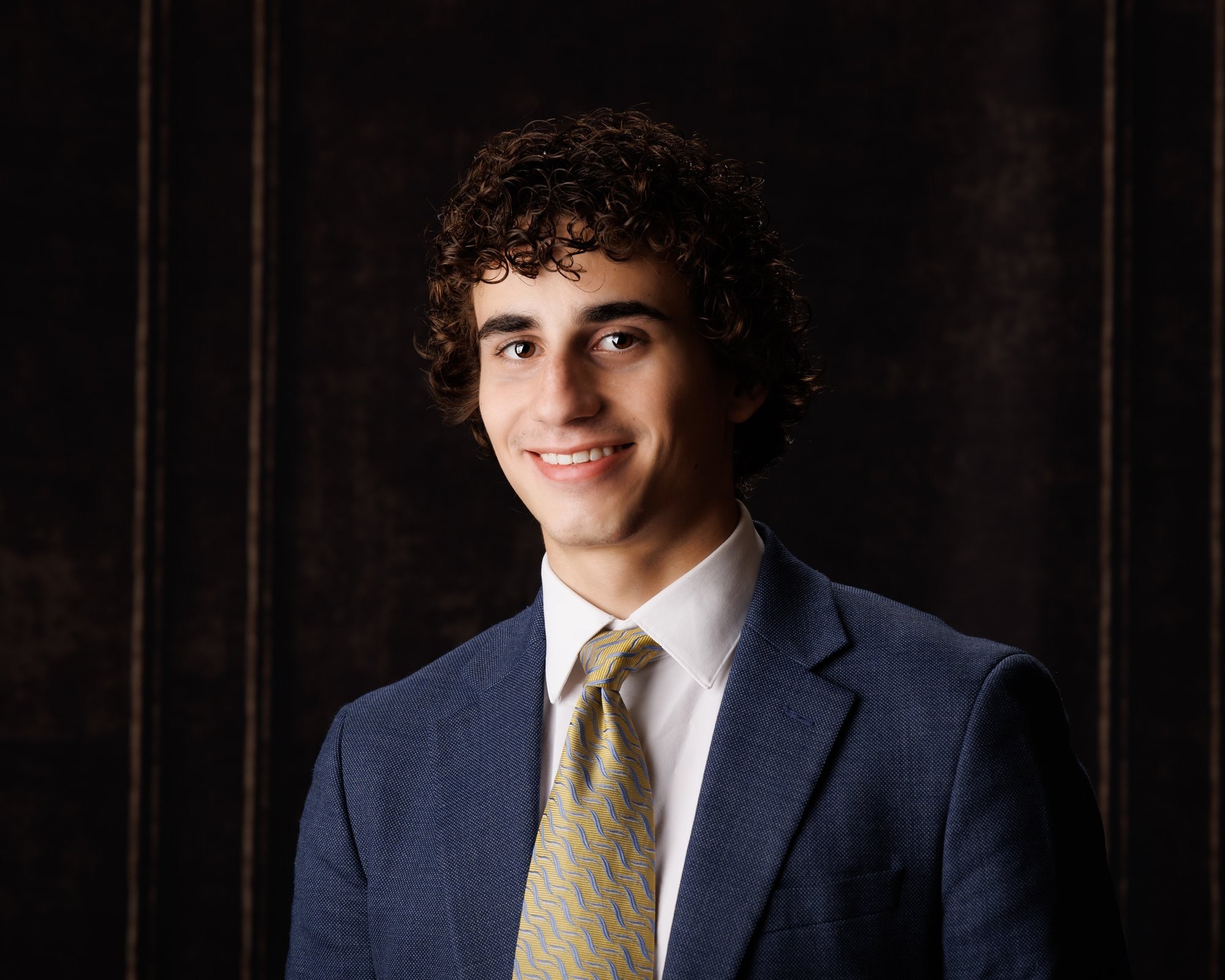 Trenton senior photography session with a young man in a blue suit and yellow tie, set against dark wooden paneling