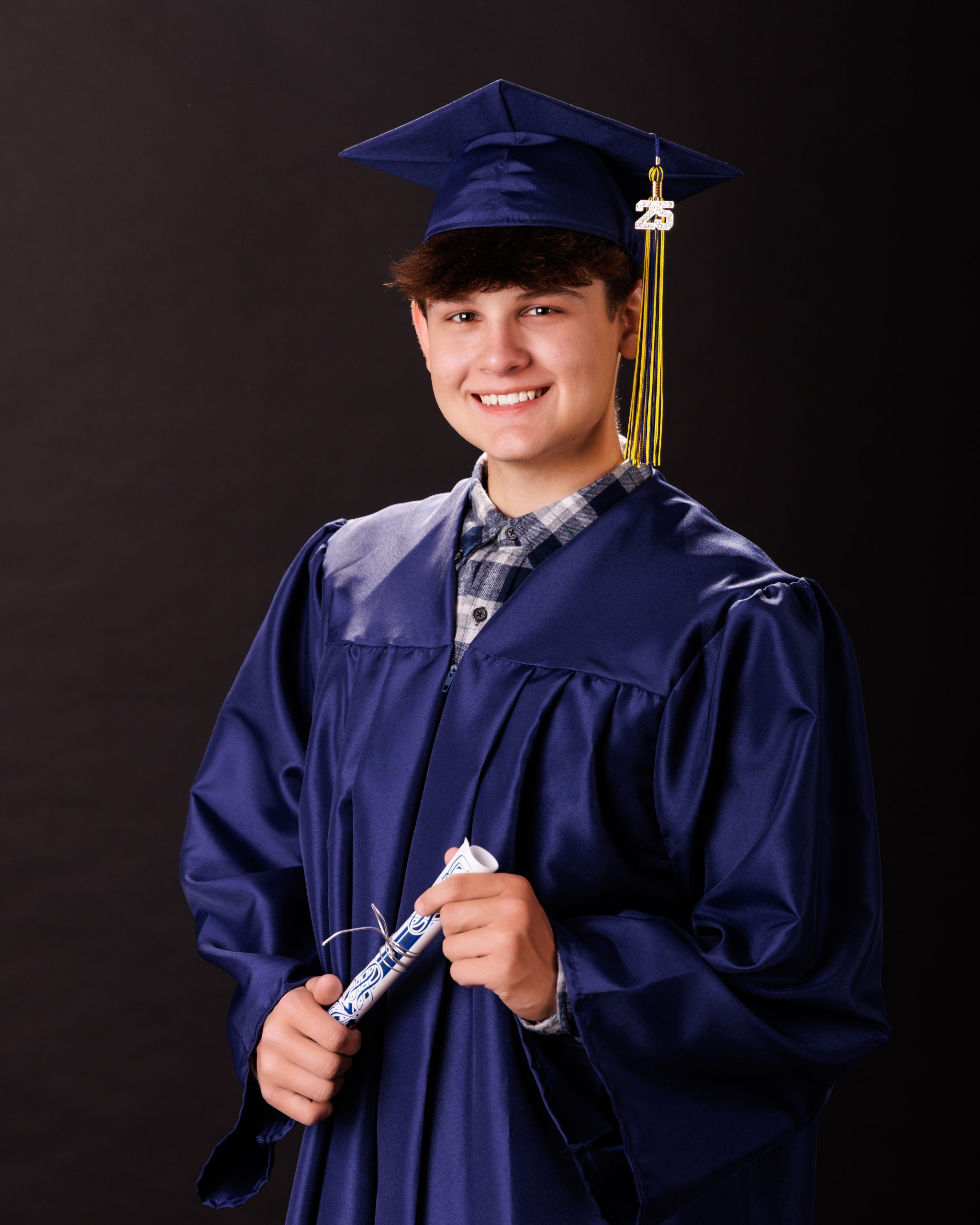 Graduation photograph of Andrew holding the 2025 sign and diploma in his cap and gown