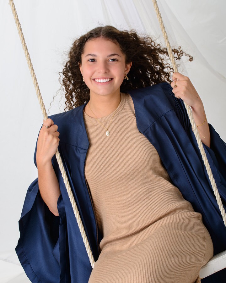 Graduate holding 'Class of 20XX' chalkboard in graduation gown at studio session