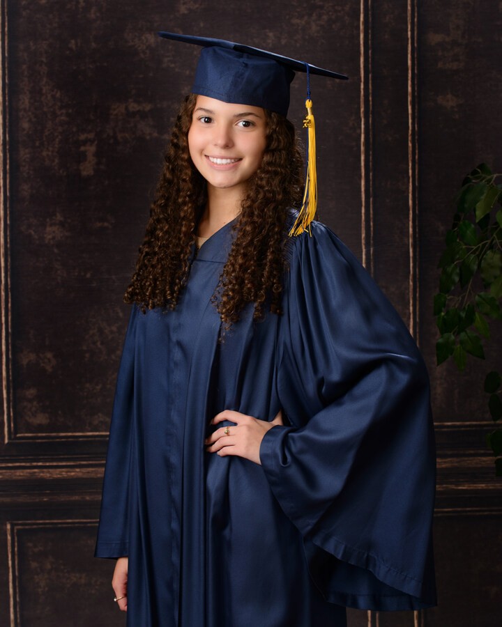 Graduate holding 'Class of 20XX' chalkboard in graduation gown at studio session