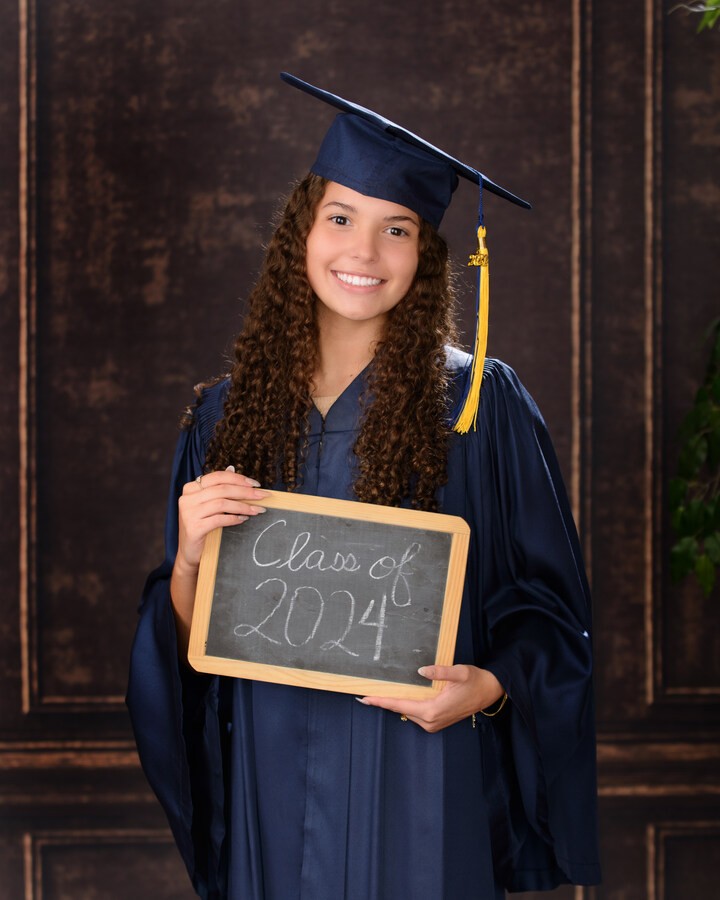 Graduate holding 'Class of 20XX' chalkboard in graduation gown at studio session