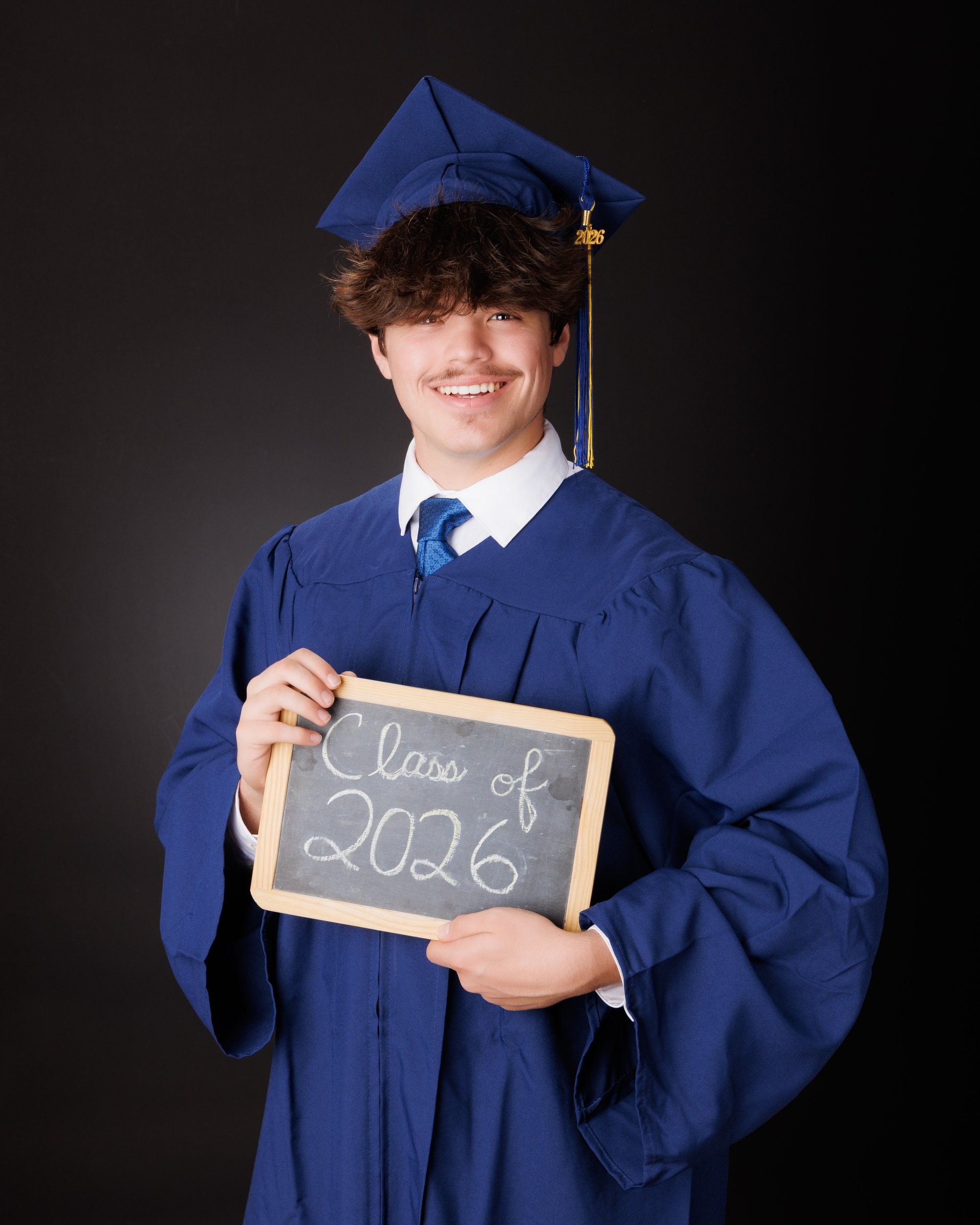 Luke in blue graduation gown and cap with 'Class of 2026' chalkboard, Downriver photo studio