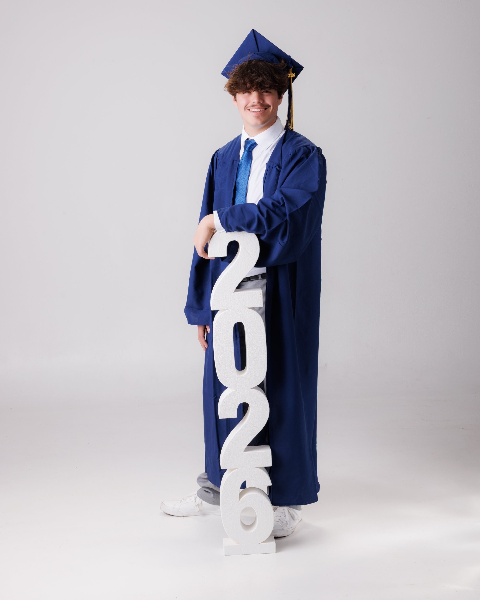 Luke in blue graduation gown and cap with 'Class of 2026' chalkboard, Downriver photo studio