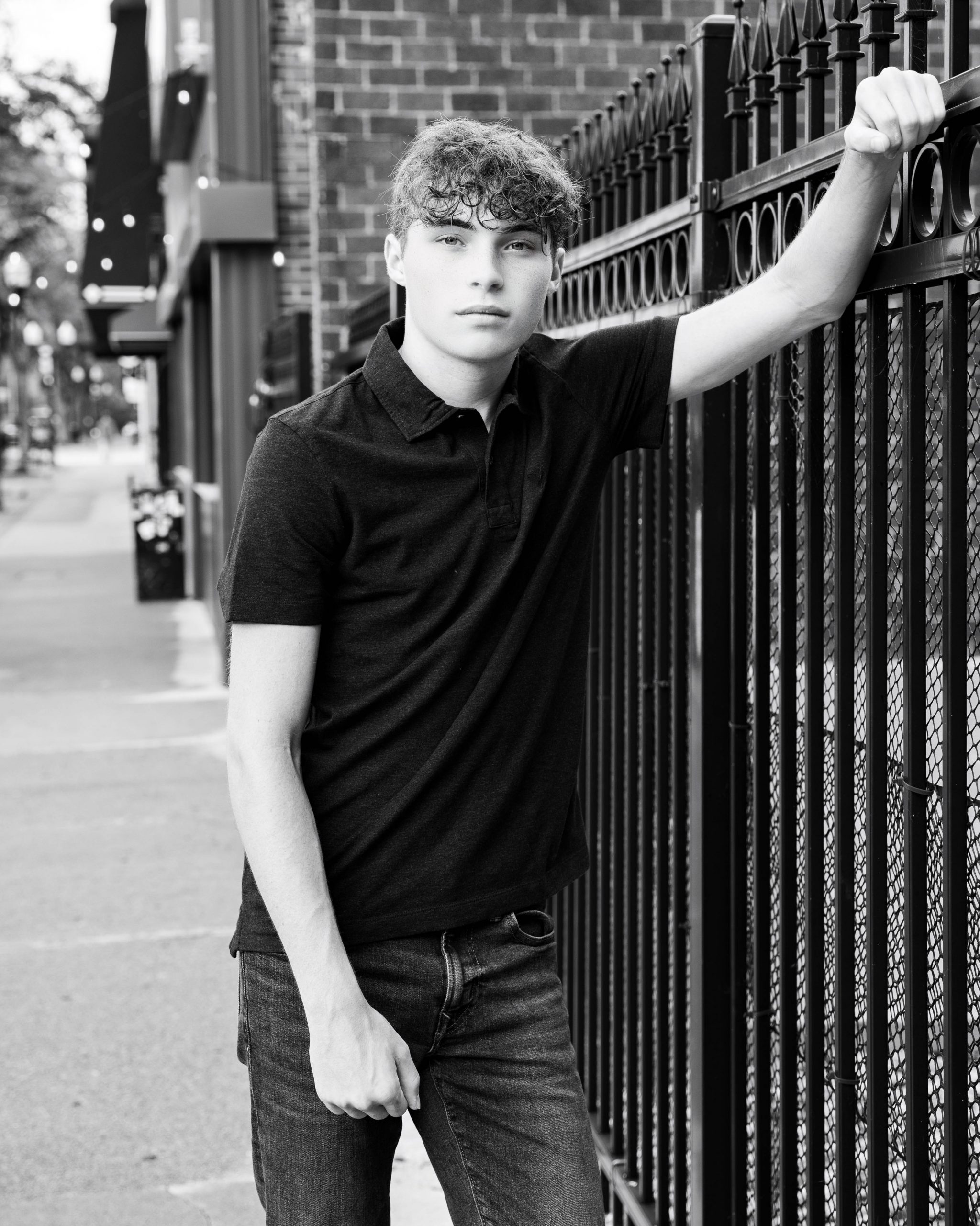 Senior portrait of Michael leaning against an iron fence on a Wyandotte street