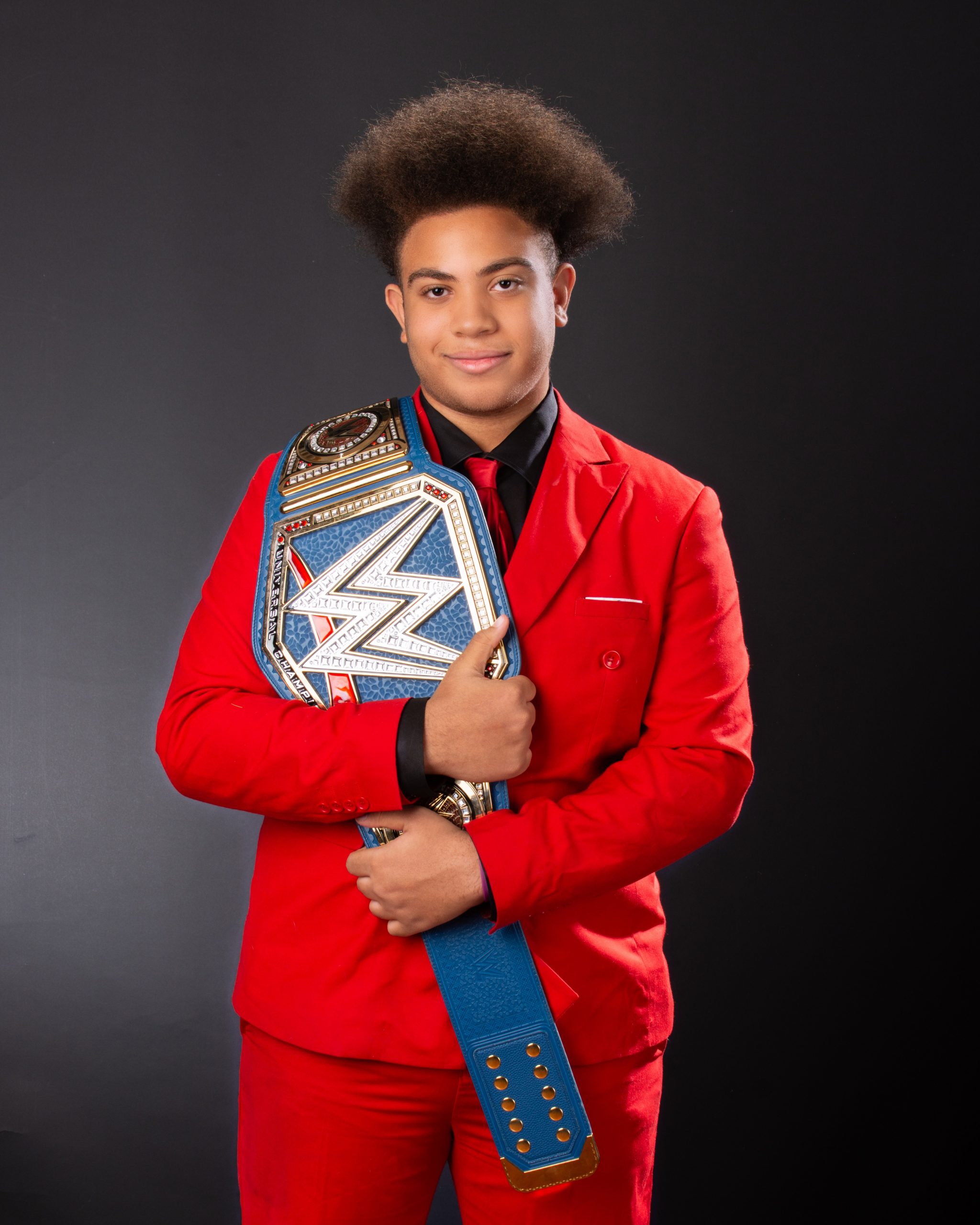 Senior photography session featuring model in red suit holding WWE championship belt