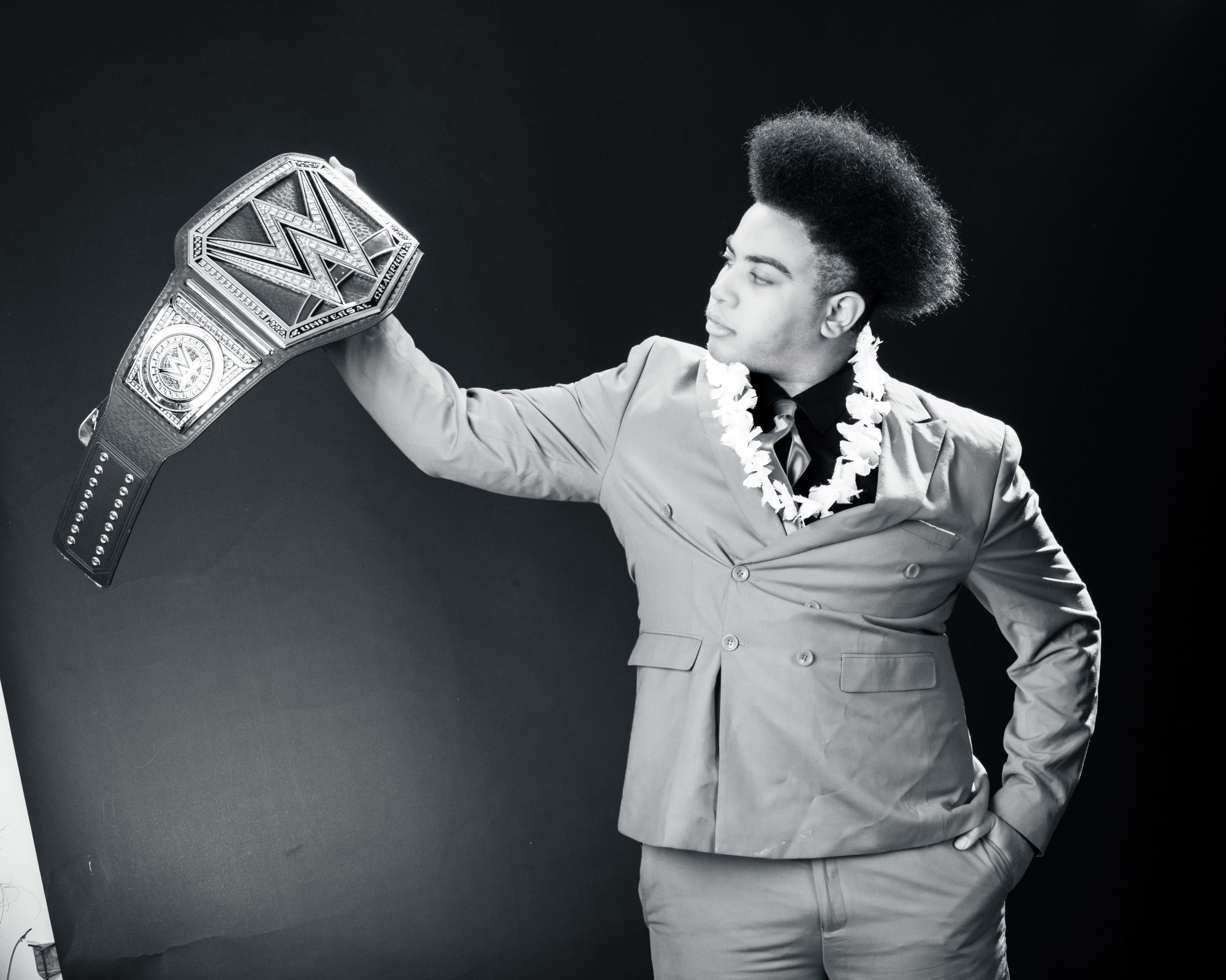 Black and white senior portrait of model wearing lei and holding WWE belt
