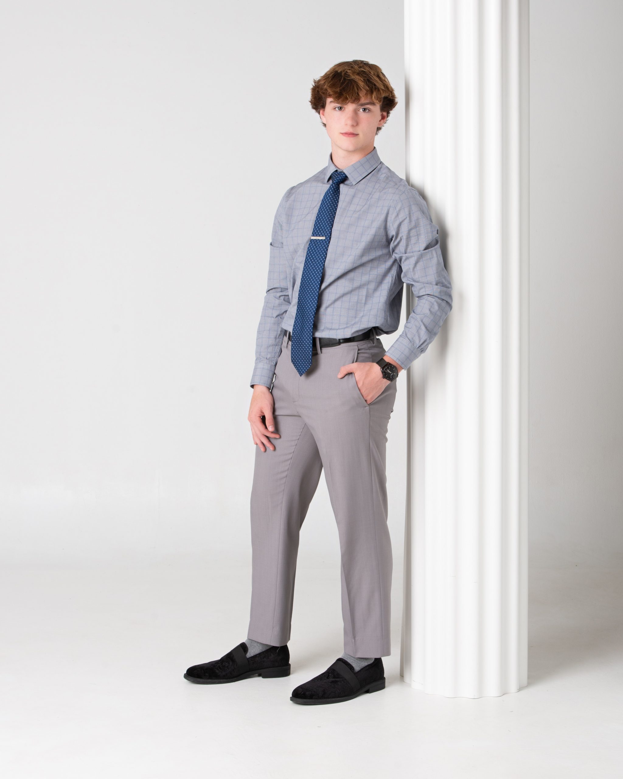 Wyandotte senior photo session portrait of a young man wearing a plaid shirt, tie, and gray pants against an orange textured backdrop