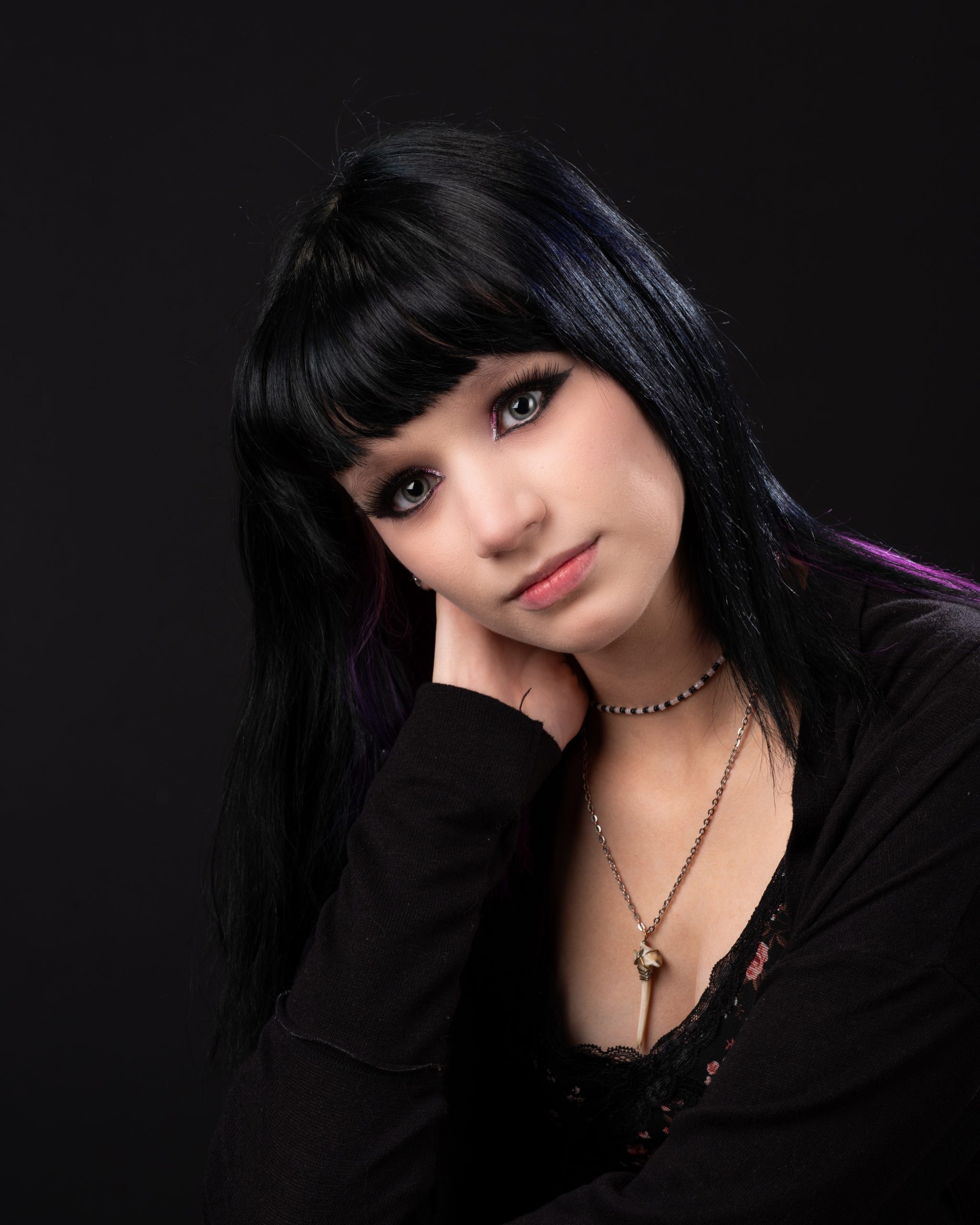 Senior girl wearing black and white striped sweater posing against dark backdrop